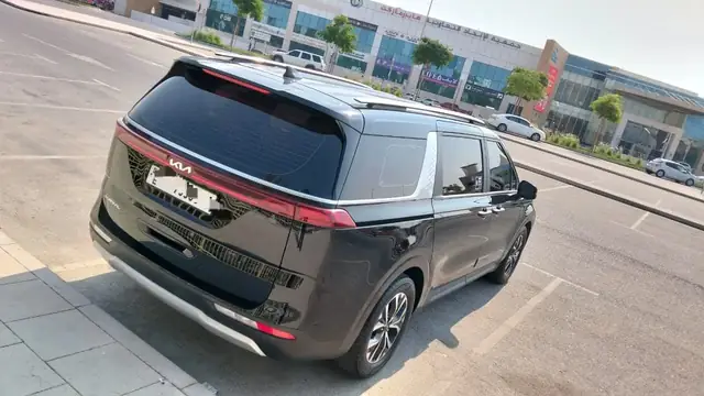 Black Kia Carnival rear view in a parking bay